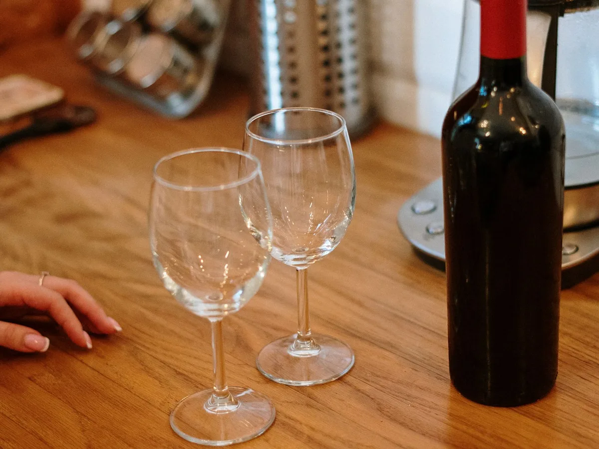 An unlabelled wine bottle and two empty wine glasses sit on a wooden kitchen counter.