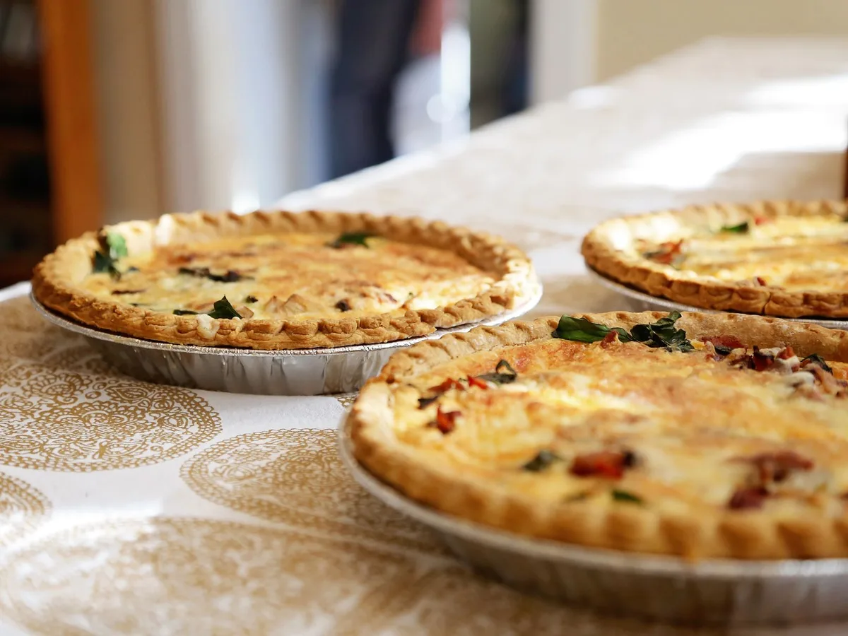 Three golden quiches in foil tins sit on a patterned tablecloth.